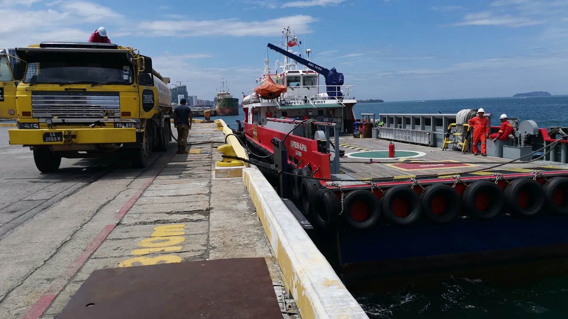 A yellow tanker truck and a red bunker vessel at the quay